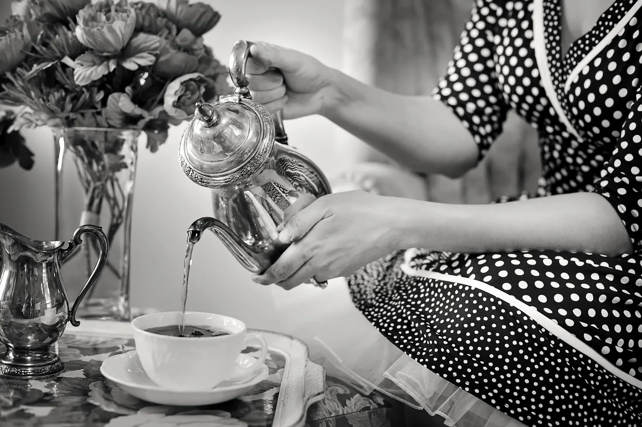 Une photo en noir et blanc de thé versé d’une théière en argent à table