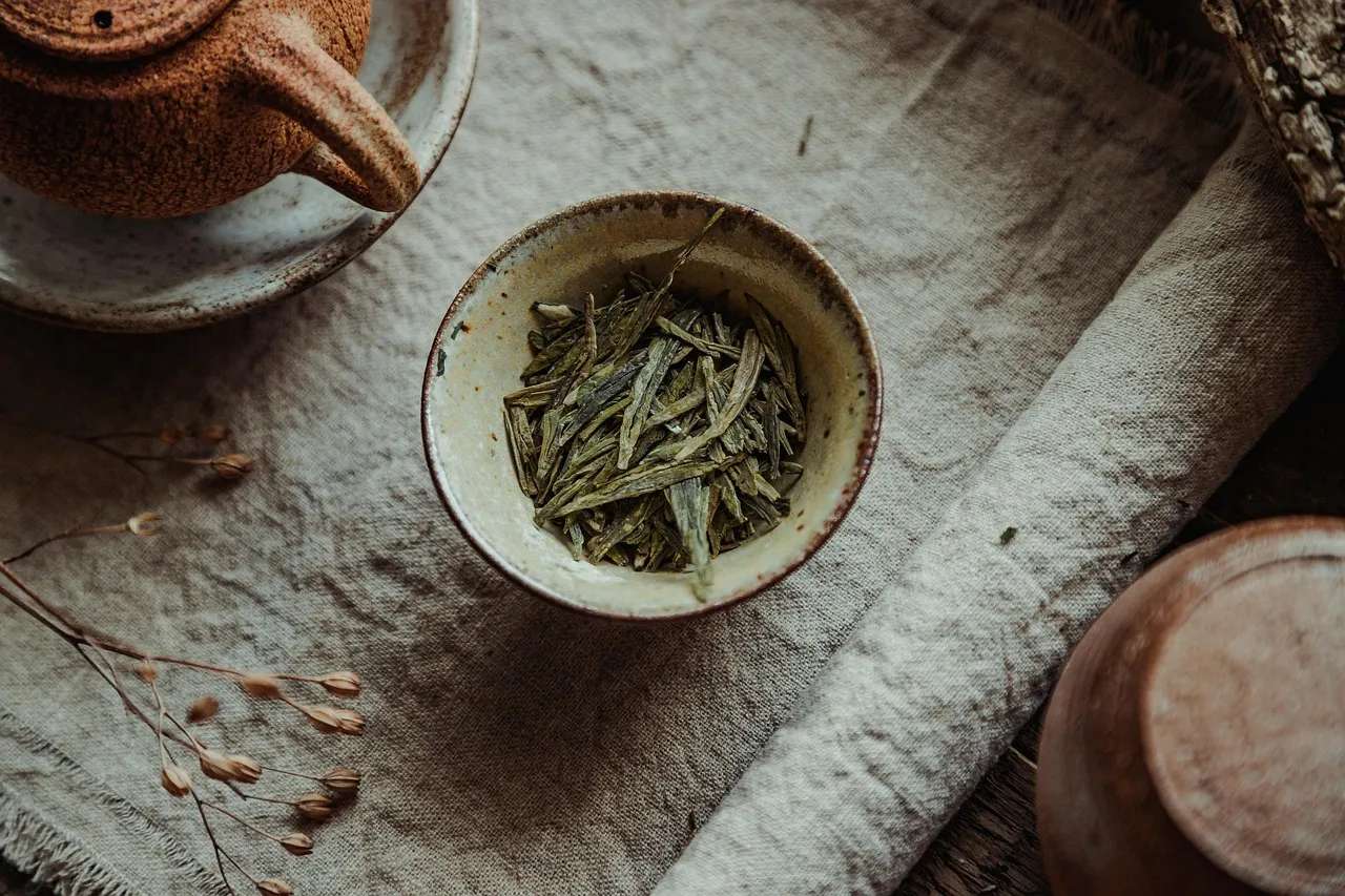 Des feuilles plates de thé vert Longjing dans un petit bol à côté d’une théière