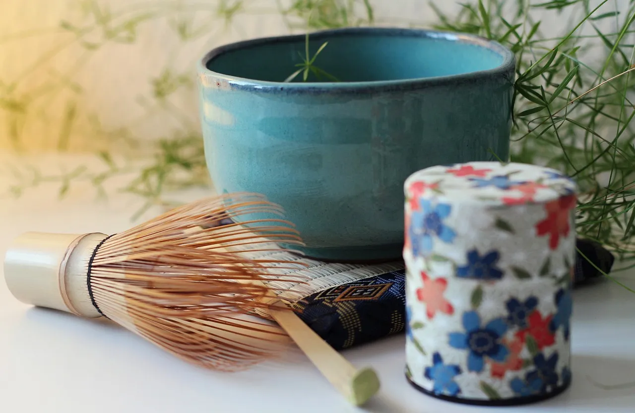 Un fouet à matcha en bambou à côté d’un bol à thé et d’une boîte à thé