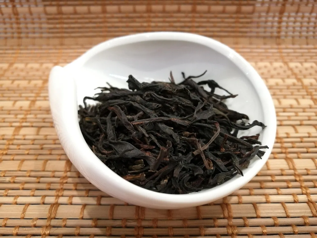 Feuilles d’oolong sombres et torsadées dans une coupelle en porcelaine blanche